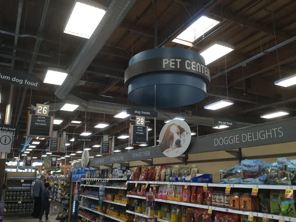 Interior de una tienda con pasillos de alimento y productos para perros bajo un letrero de sección de mascotas