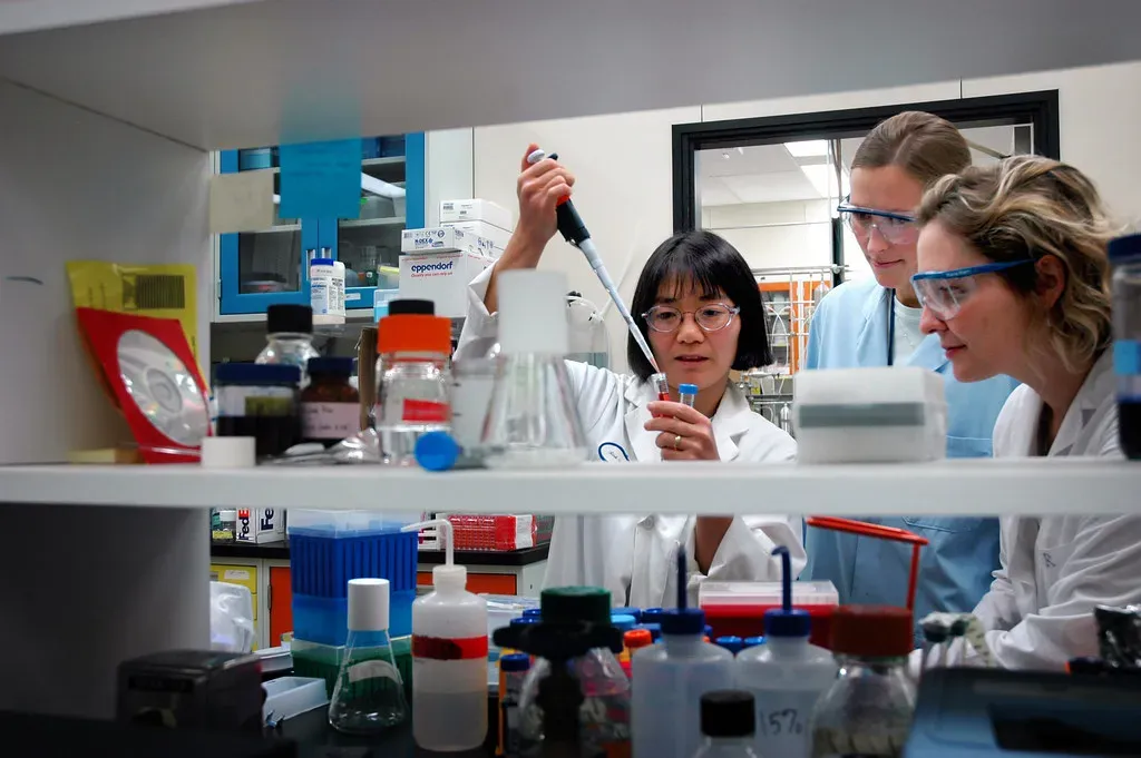 Mujeres científicas con delantal trabajando en un laboratorio, vistas entre estantes con frascos